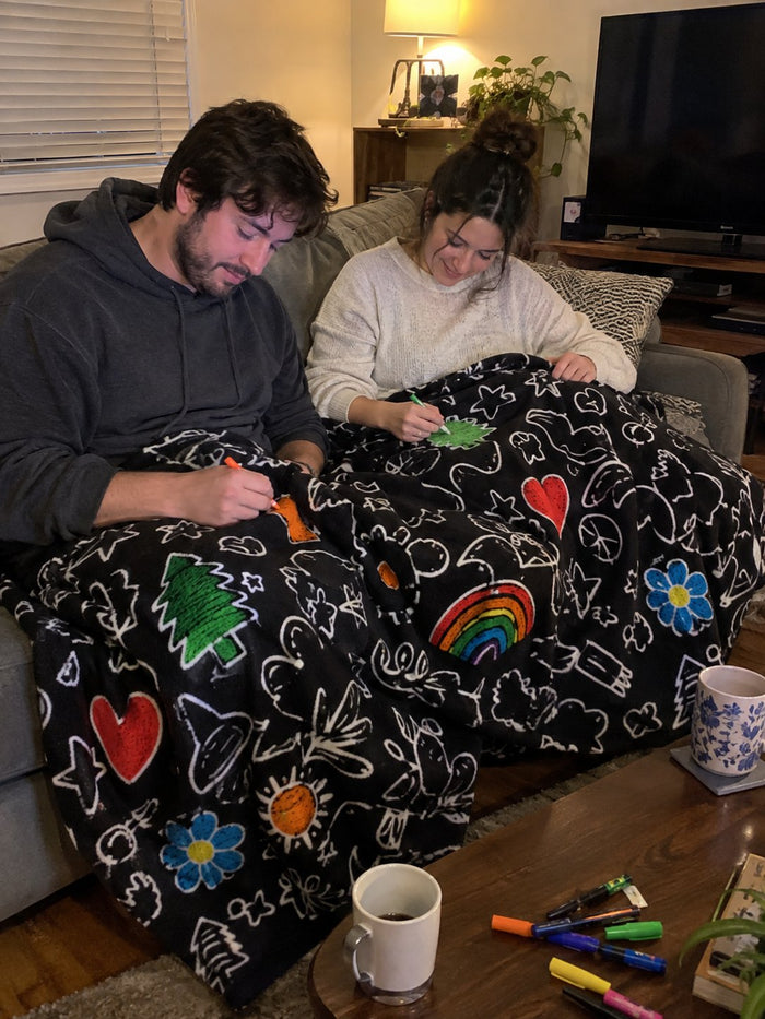 A couple under the blanket on the sofa, each coloring a different corner