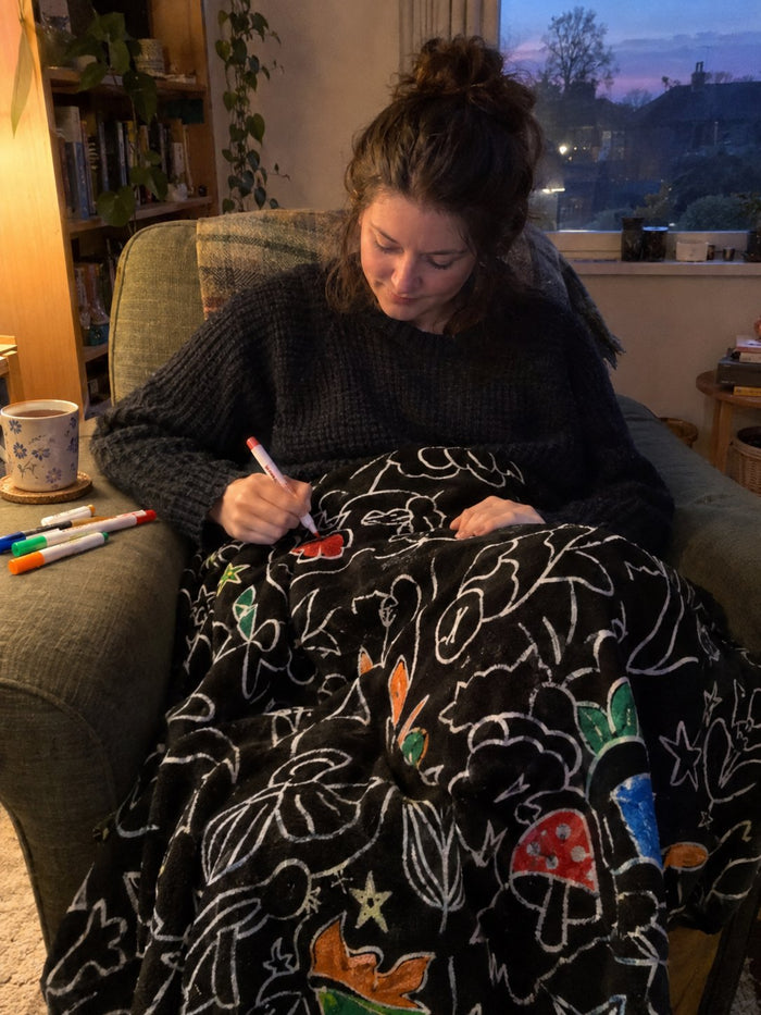 A woman in an armchair at dusk with the blanket over her knees